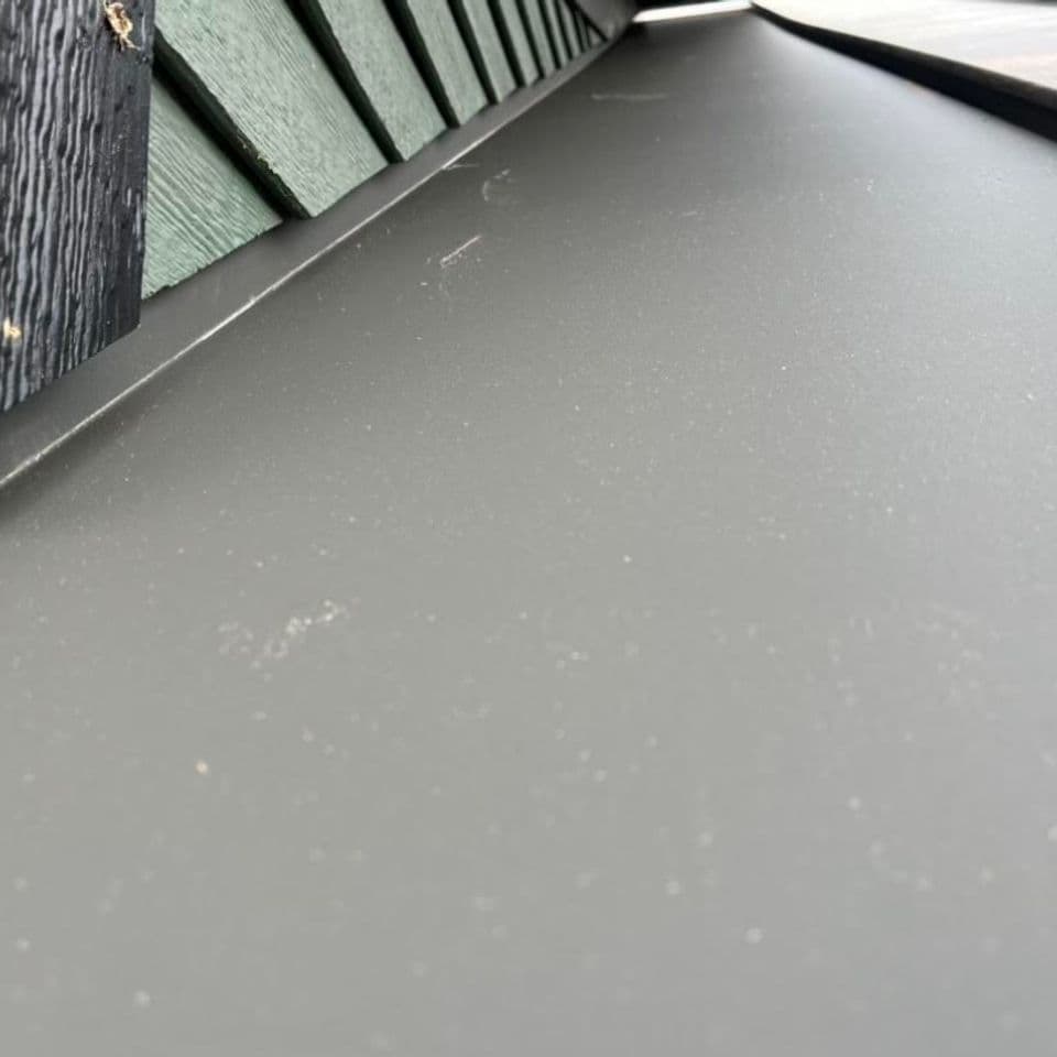 Close-up of a sleek, gray metal roof edge against a wooden wall.
