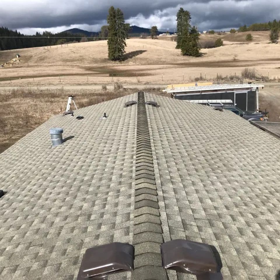 Roof view showcasing shingle texture, drainage pipes, and scenic mountainous landscape.