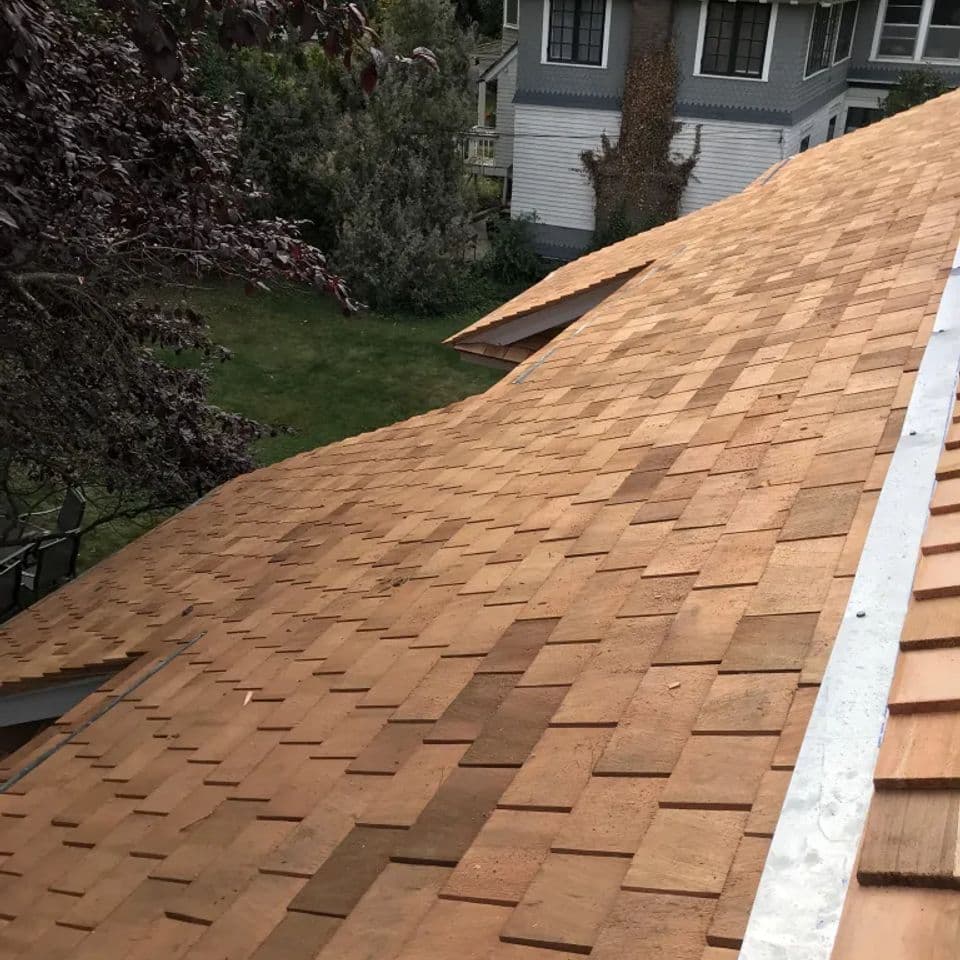 New wooden shingle roofing installed on a sloped house, showcasing craftsmanship and design.