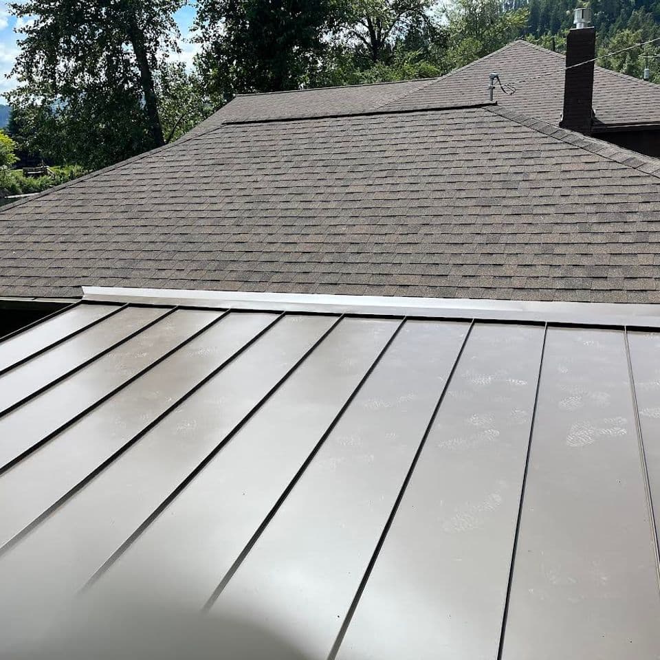 Metal roof installation over a residential home with neighboring rooftops and trees in the background.