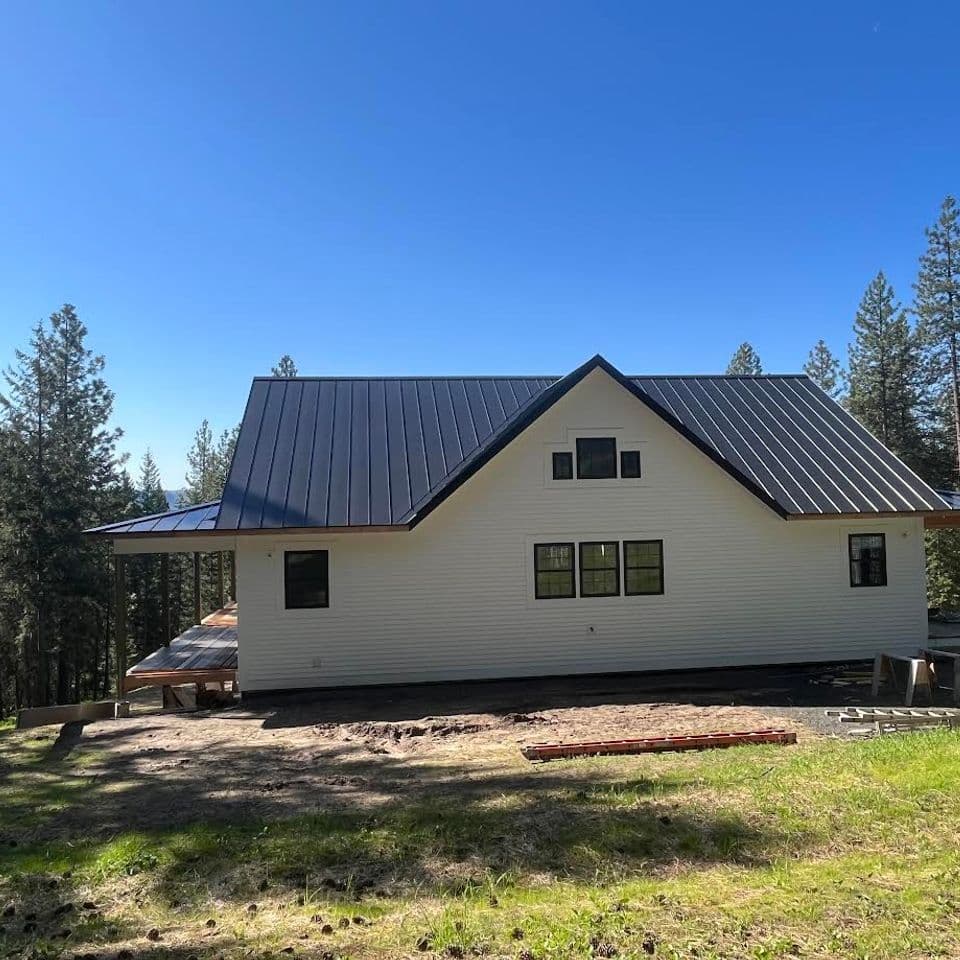 Modern hillside home with a metal roof and large windows, surrounded by trees.
