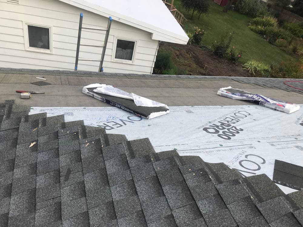 Roofing installation with underlayment and shingles laid out on a house roof.
