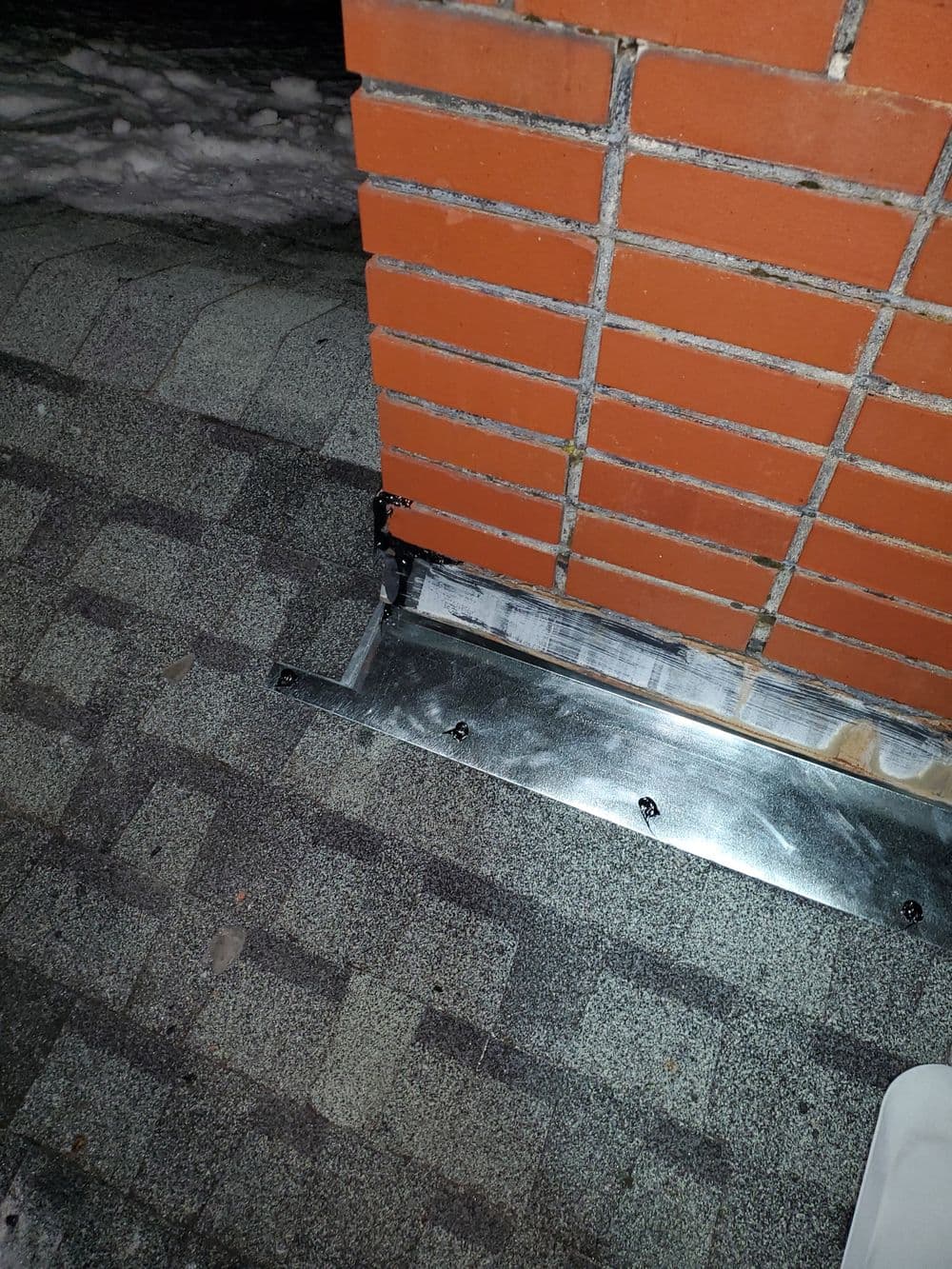 Close-up of metal flashing installed at the base of a brick chimney on a roof.