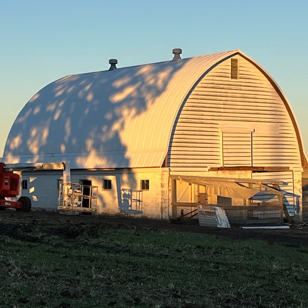 Rainy season barn with arched roof and construction materials outside, bathed in golden sunlight.